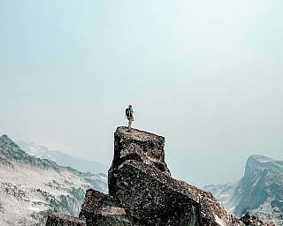 Ein Wanderer steht auf einem felsigen Gipfel mit Blick auf eine bergige Landschaft.