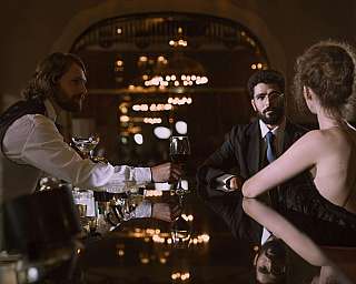 Ein Barkeeper serviert Wein an zwei Gäste in einer stilvollen Bar.