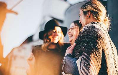 Drei Frauen lachen und teilen einen fröhlichen Moment im Freien.