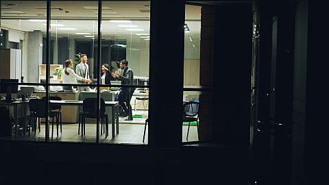 Vier Personen feiern in einem modernen Büro bei Nacht.